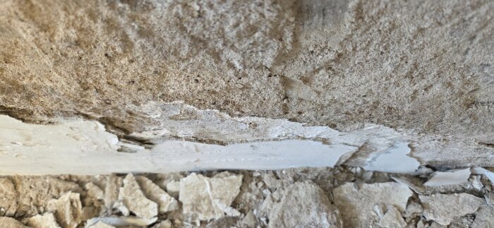 Närbild av vägg med löst putssläpp i källare, vit cementbaserad lappning synlig bland bruten gammal puts.