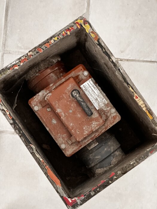 Röd ventil med handtag och märkningar "REDI" och "LGA" på rör i källargolv. Handtag med lägena Open och Closed, potentiell funktion för vattenstängning.