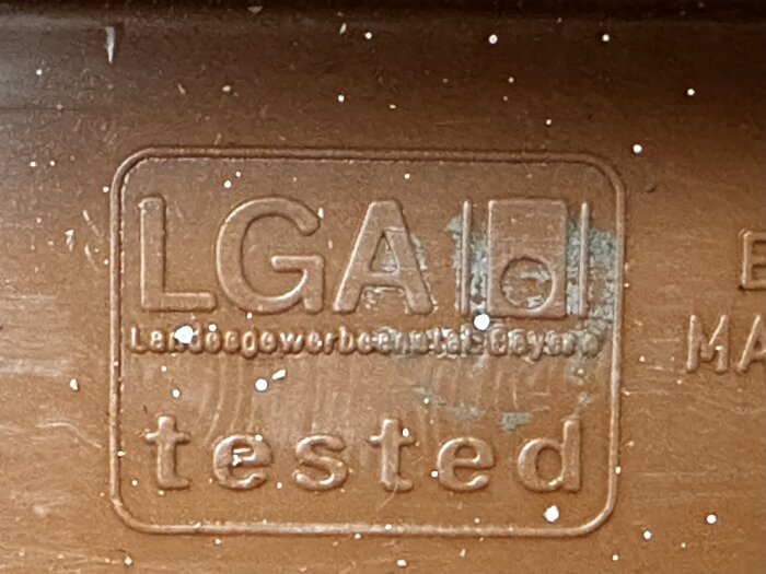 Brunt rör med präglad text "LGA tested", slitage och vita prickar syns, del av ett system som kan innefatta ventiler eller backventil.