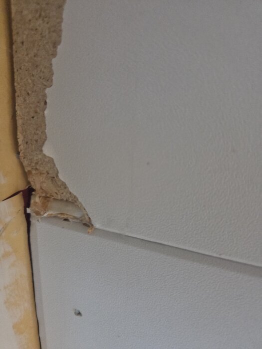 Skadad innertakskiva med synligt lager av material, visar hål och skrapan vid kanten på en vägg.