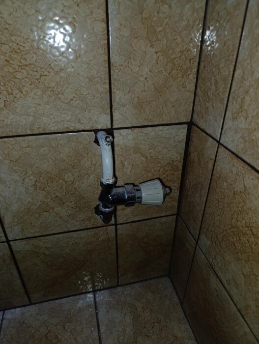 Vinklad väggrörsanslutning utan radiator, brun kakelplatta bakom.