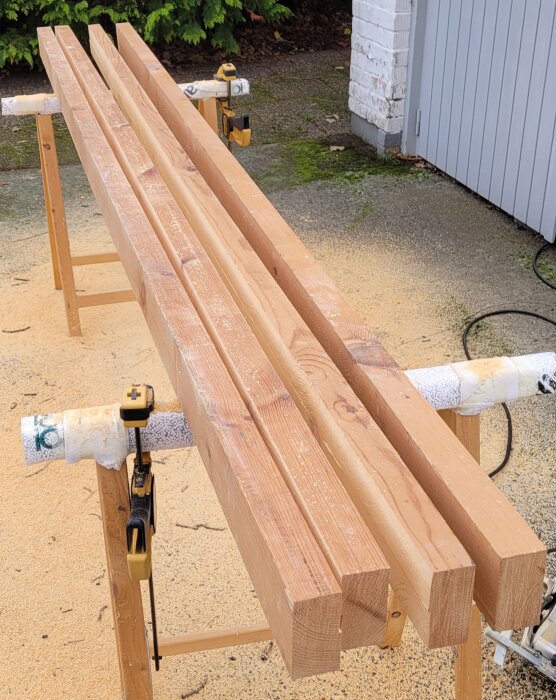 Fyra träplankor på sågverktyg utomhus redo för kapning.