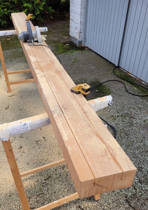 Bild på en planka som kluvs med cirkelsåg, placerad på bockar utomhus. En gul måttenhet syns bredvid.