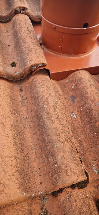 FTX installeringstakhuv på tak, vänster sida under tegelpanna. Huv problematiskt placerad, sitter löst. Rustikt, mossigt tak med orange tegelpannor.