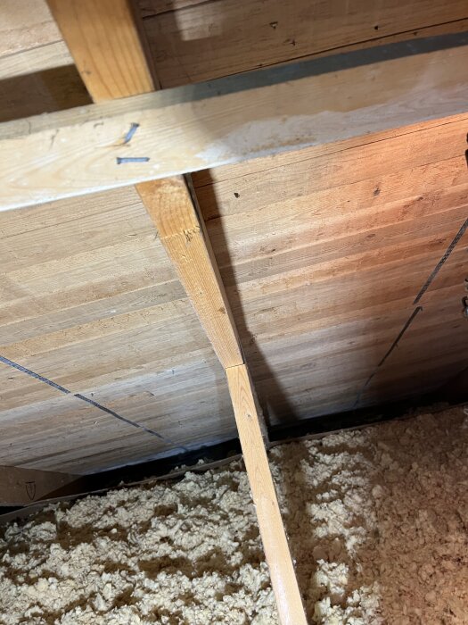 Trätak med vita fläckar och isoleringsrester synliga på tvärreglar, angränsat av träreglar, i ett utrymme med hög luftfuktighet.