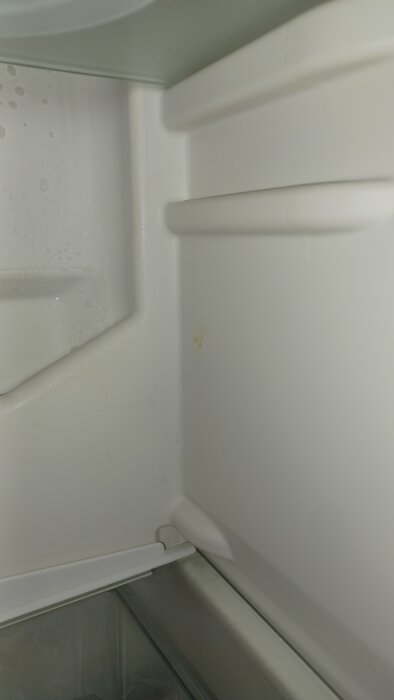 Inre hörn av kylskåp med kondensbildning på väggen.