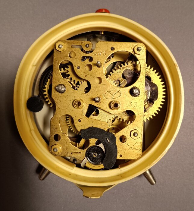 Baksidan av en gammal väckarklocka med synliga kugghjul och mekanik från en urfabrik i Rostov na Donu, klar för rengöring och smörjning.
