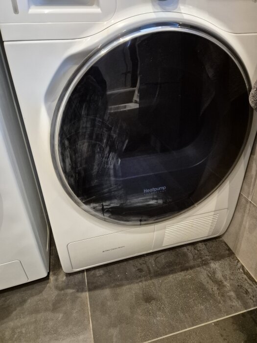 Torktumlare med svarta och vita fläckar på luckan efter användning av nagellacksborttagning. Golvet är mörkt och luckan stor och rund.