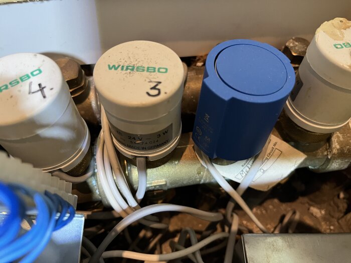 Termostater och ventiler från Wirsbo monterade på ett rör med märkningar och kablar.