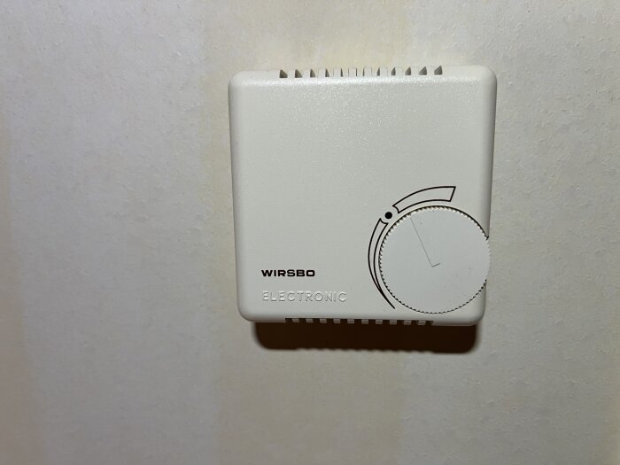 Termostat på väggen med vred, märkt "Wirsbo Electronic".