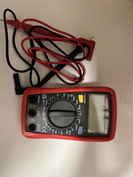 Multimeter med röda och svarta kablar, ratt för inställningar och display.