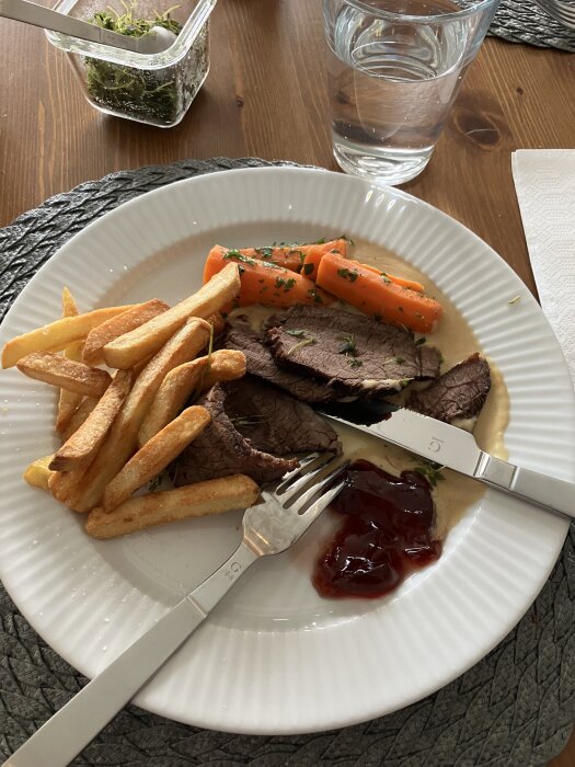 Söndagsstek med pommes frites, kokta morötter, gräddsås och gelé på en tallrik.