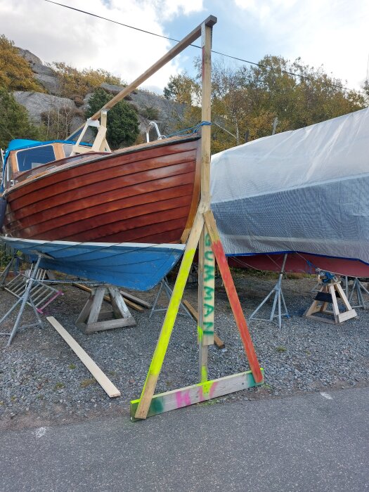 En båt på land med en täckställning av trä kan ses, omgiven av grus och träd i bakgrunden.