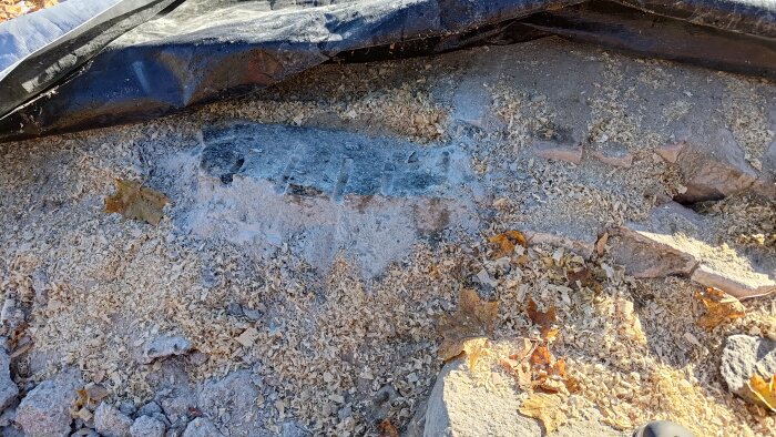 Spruckna stenar ovanpå jordkällaren täckta med sågspån och döda löv under en svart presenning.