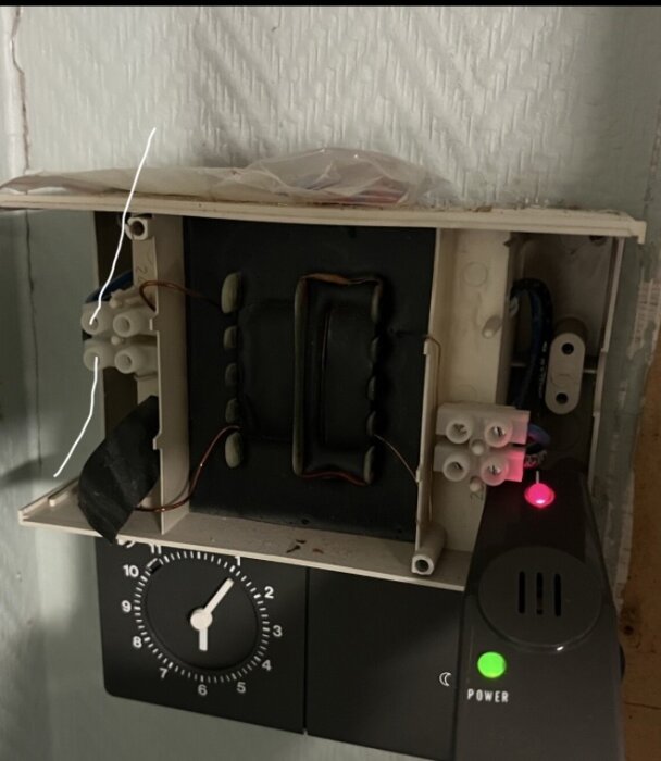 Öppen elektrisk kopplingsbox med synliga trådar och skruvkontakter bredvid en timer och enhet med indikatorlampor för ström och status.