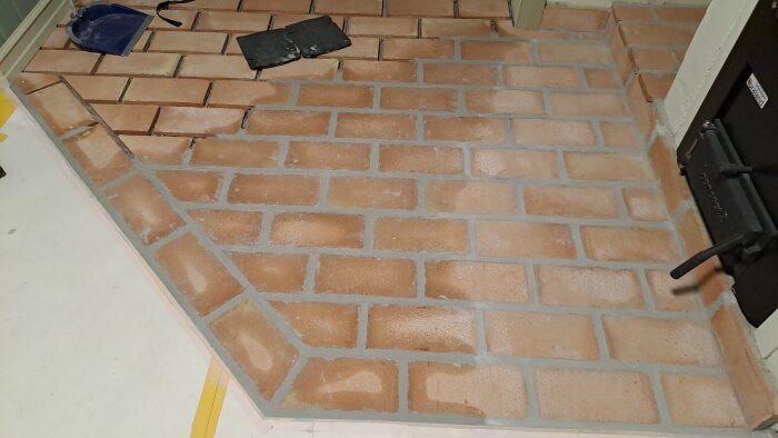 Tegelgolv nära färdigfogning med städverktyg bredvid. Golvet är ofärdigt och har nyligen blivit fogat inför sotarens besök.