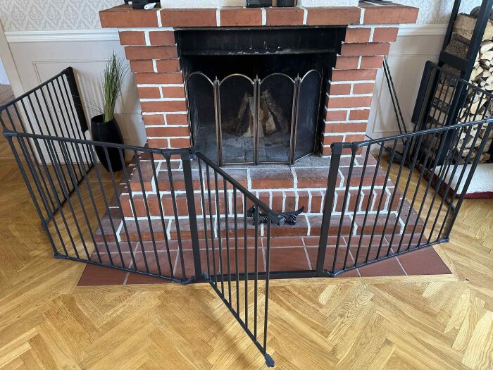 Öppen spis i röd tegel med svart galler framför, placerad i vardagsrum med trägolv.