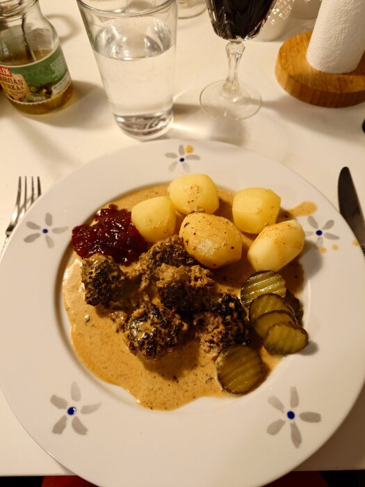 Köttbullar med potatis, brunsås, smörgåsgurka och lingon på en tallrik.