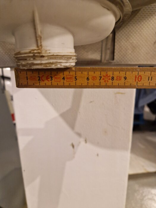 Utloppsröret på en gammal utslagsback med en linjal som mäter dess diameter, vilket är större än standardmått för vattenlås.