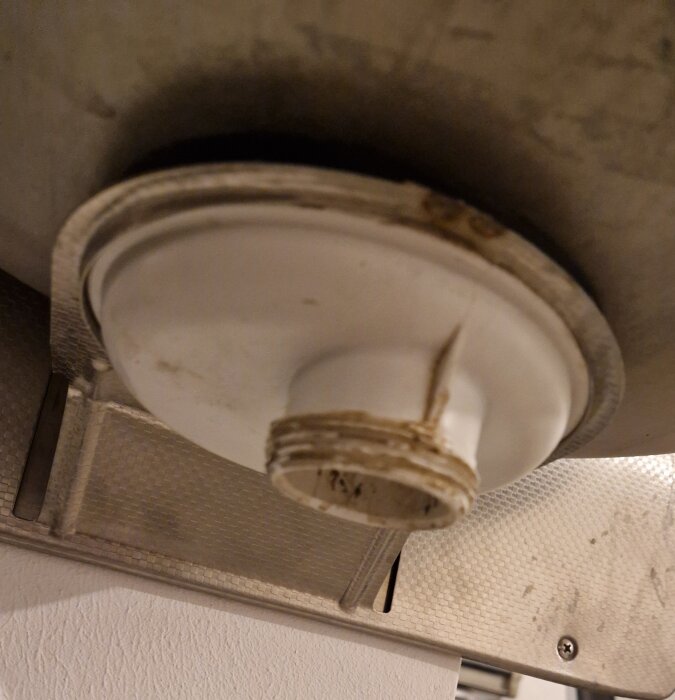 Närbild av undersidan av en gammal utslagsback med synligt avlopp och skadad anslutning.