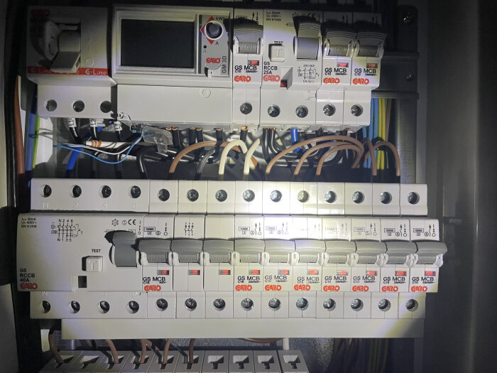 Elcentral med säkringar och brytare, delvis belyst, visar märkning och kablage i en installationspanel.