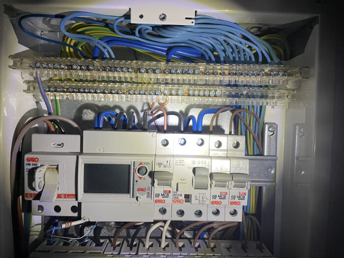 Elektrisk central med automatsäkringar och kopplingskablar i olika färger, upplyst i trångt utrymme.