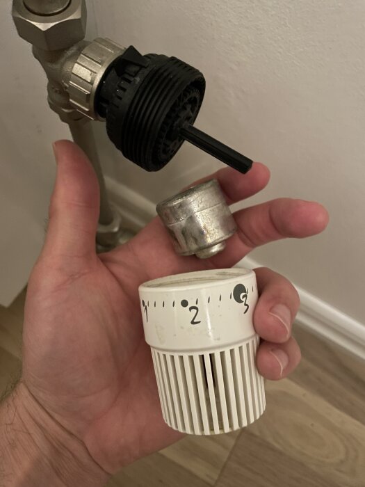 En hand håller en löstagbar termostatventil från ett element; ventilen är tillverkad av plast och metall, inställbar från 1 till 3.