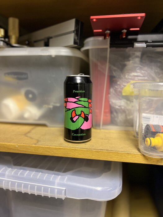 Ölburk med färgglad etikett på en hylla i ett garage, omgiven av plastlådor och verktyg.