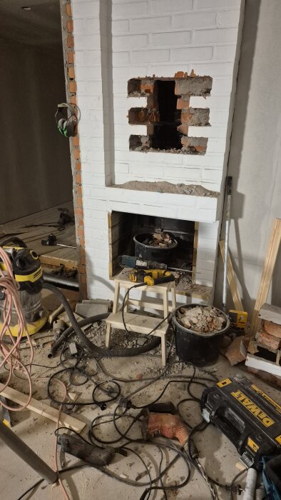 Renoveringsprojekt med öppen spis under arbete, omgiven av verktyg och byggmaterial.