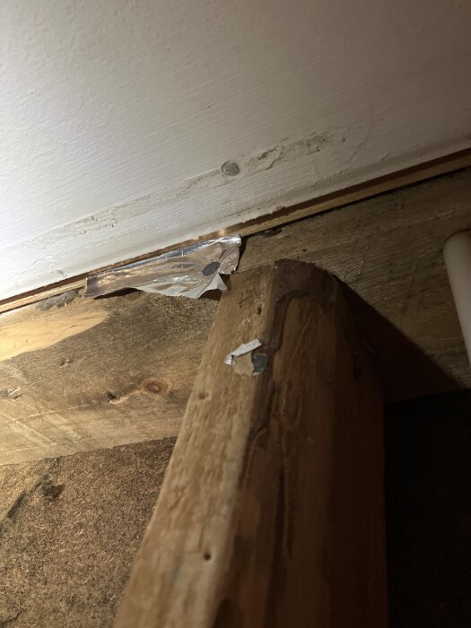 Träregel med rester av silvrig folie nära innertak i ett hus med tegelfasad.