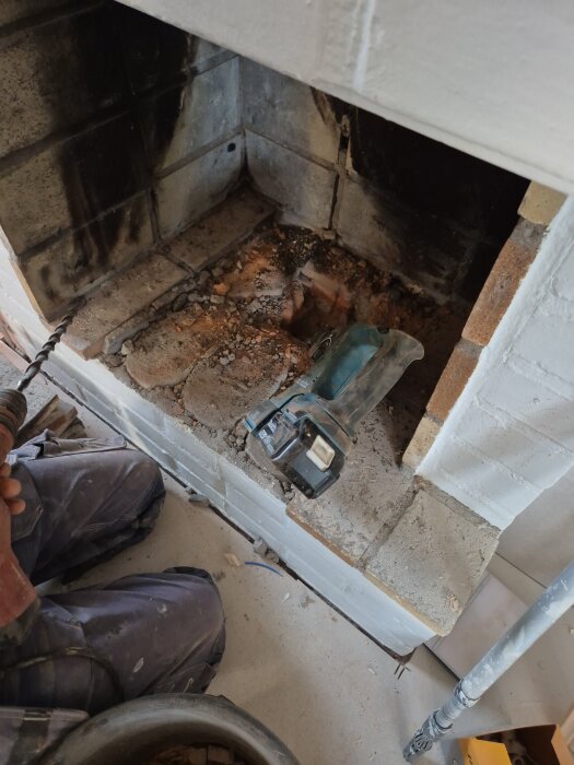 Öppen spis med delvis bilad botten för tilluftsinstallation, en borr och verktyg synliga, förbereder sig för tilluftsrör och målning.