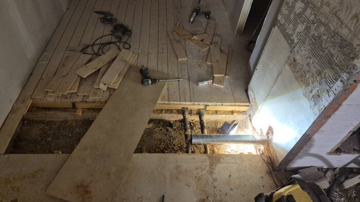 Renovering av golv med uppbruten golvyta, brädor, borrmaskin och ett nytt ventilationsrör installerat för kaminens tilluft.