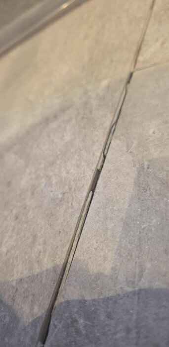 Sprucken fog mellan klinkerplattor i badrummet på grund av sjunkande plattor, synligt i duschområdet.