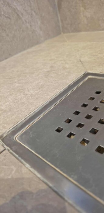 Duschbrunn med sjunkna klinkerplattor och sprucken fog i ett nyrenoverat badrum.