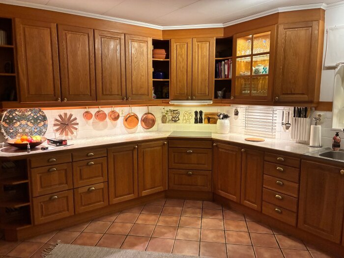 Kök med Tibrokök skåpluckor i oljad ek, diskbänk med kopparkastruller och keramiska dekorplattor, samt belysning under skåp.