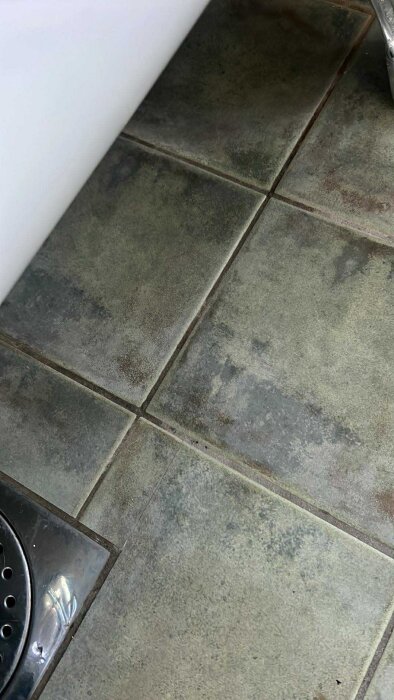 Klinkergolv i badrum med tecken på fukt och vatten runt golvbrunn; ingen synlig läckagekälla från badkar eller avloppsanslutningar.