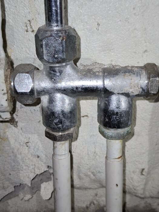 Rörkoppling från ett vattenelement i ett en-rörssystem, sett mot en vit vägg, med två anslutna vita rör under.