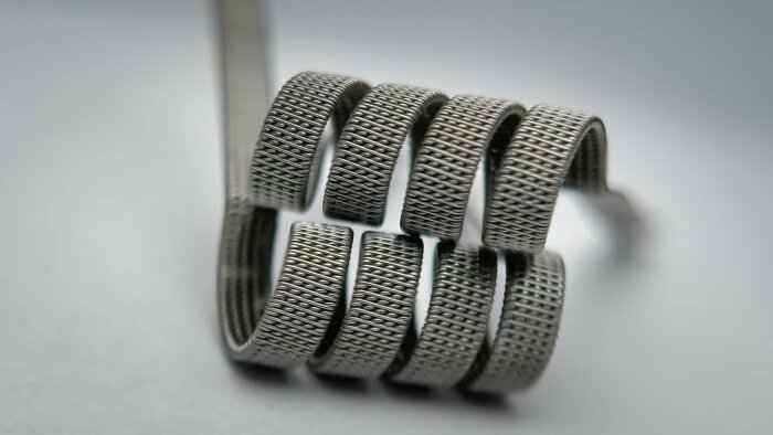 Närbild på en komplex clapton coil för vaping, där tunna nichrome-trådar är fint lindade runt en kärna, vilket liknar en gitarrsträng.