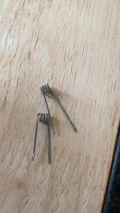 Tre handgjorda vape-coils av metalltråd på ett trägolv.