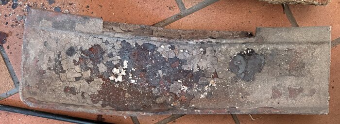 Sliten och sprucken rökhylla från en Morsö 4132 kamin, liggandes på golv. Finns skador och avflagningar på ytan.