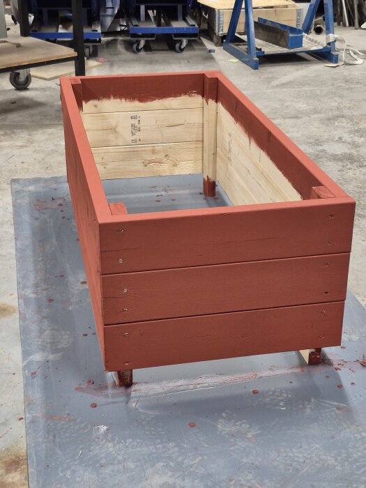 Upphöjd, rödbrun, trälåda med ben utan botten, i verkstadsmiljö.