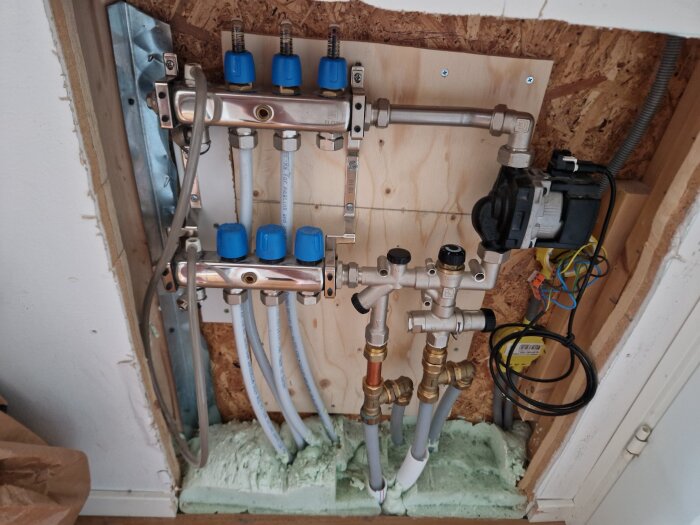 Golvvärmeinstallation med rördragning och ventiler, synliga blå reglerventiler och krets för uppvärmning på våning/entreplan, utan termometer.