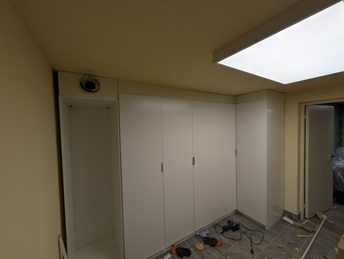 Vitt skåpsystem installerat i rum, med öppna dörrar och en ofärdig hylla, verktyg ligger på golvet, redo för lister.