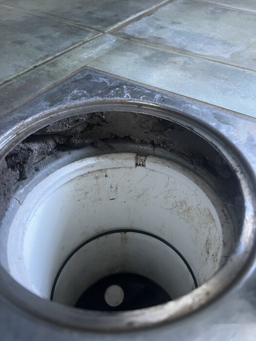 Badrumsgolv med en brunn, mattan har inte spruckit vid vikning, kakelplattor syns runt brunnen.