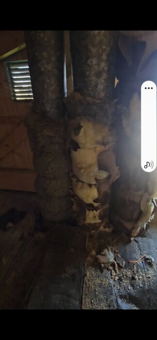 Oisolerade ventilationsrör med skadad isolering i ett vindsutrymme, synlig trävägg i bakgrunden.