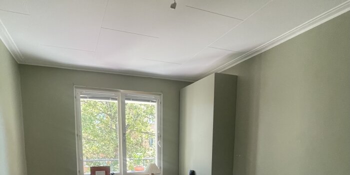 Ett rum med gröna väggar, vitt tak och ett fönster med utsikt mot grönska.