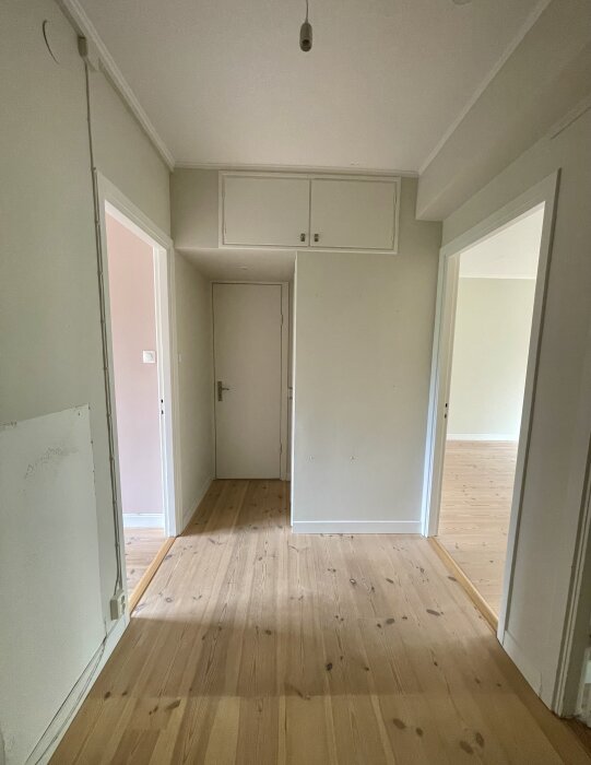 En hall i neutral färg med trägolv, två dörrar och ett mindre överskåp syns, del av renoveringsprojekt i hemmet.