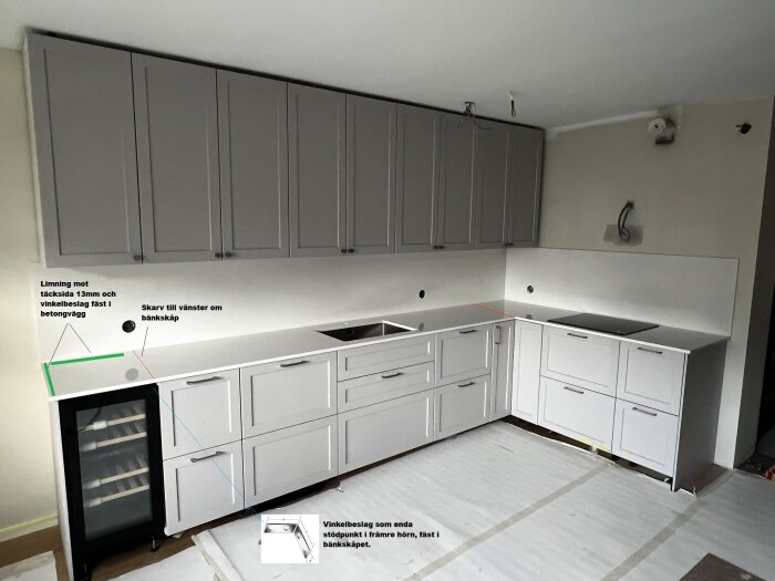 IKEA-kök med grå skåp, vit bänkskiva och väggplatta av kompositsten. Markeringar visar skarvar och vinkelbeslag ovanför vinkyl.