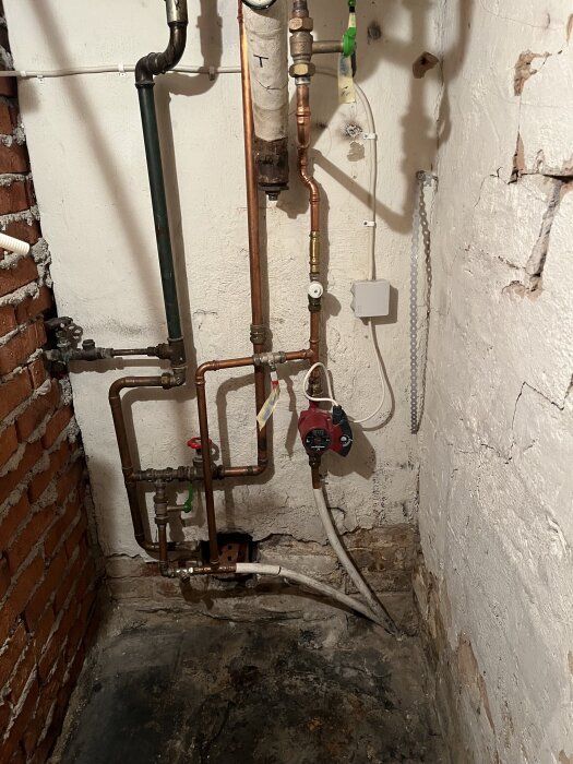 Rörinstallationer i hörn av källare, vissa är kopplade till en pump och markeringar på rör, i fråga om koppling och temperaturreglering.