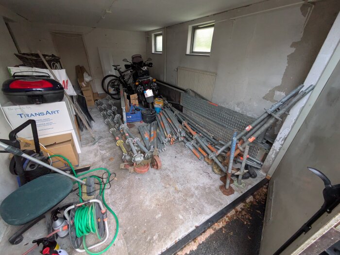 Garage med byggställningar, kartonger, cyklar och andra redskap. Ställningar nyligen köpta och placerade på golvet.